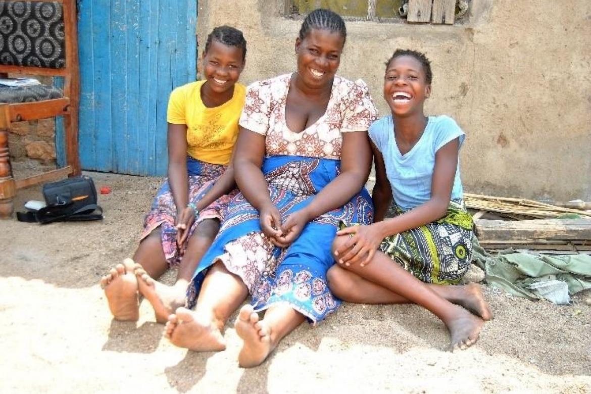 Yankho, assise devant la porte de sa maison avec sa soeur jumelle Pemphero et sa maman. Sur la chaise derrière elles se trouve une partie de leur matériel d'apprentissage. Crédit : UNICEF Malawi/2020/Gondwe