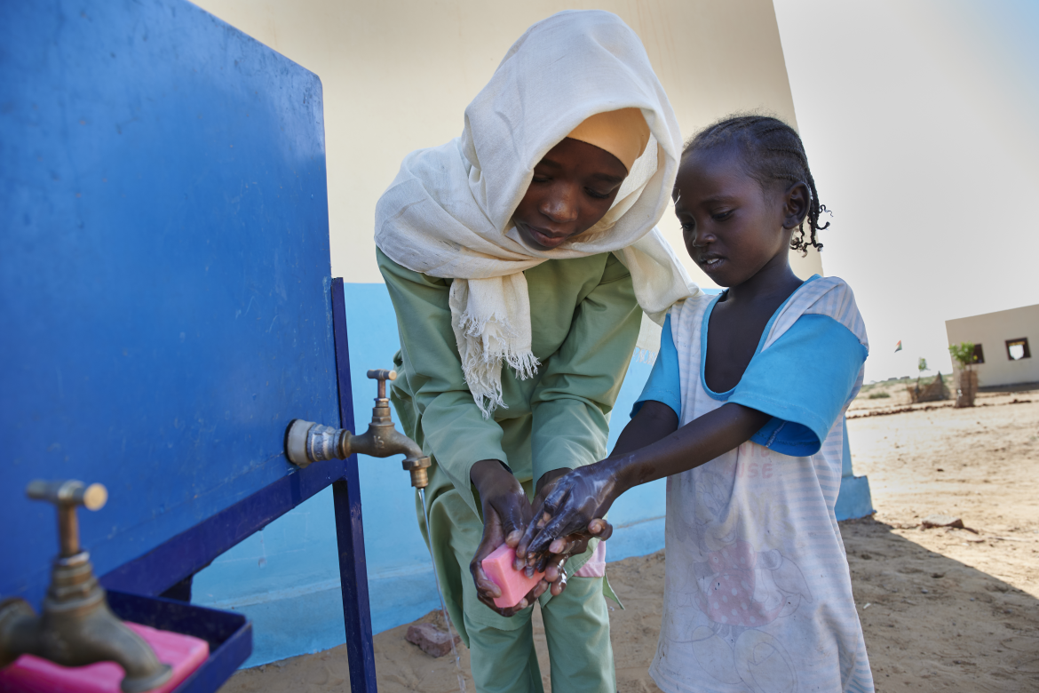 Une jeune fille montrant à une élève de maternelle comment bien se laver les mains avec de l'eau et du savon. École Ban Jadid à El-Fasher au Nord Darfour. Soudan (2019). Crédit : UNICEF/Noorani/UNI233850